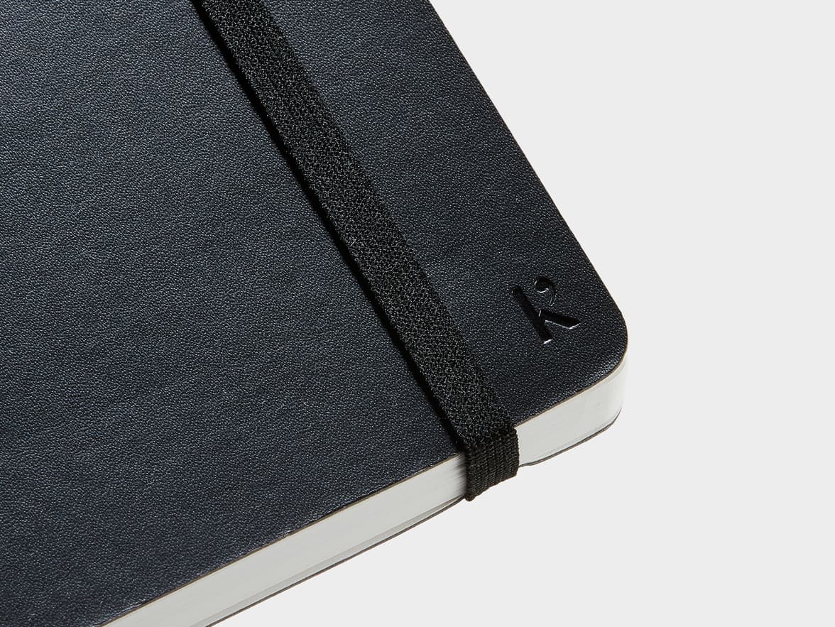 Close up shot of the corner of the cover of the Black Karst Stone Paper  Softcover Notebook with Karst branding and strap