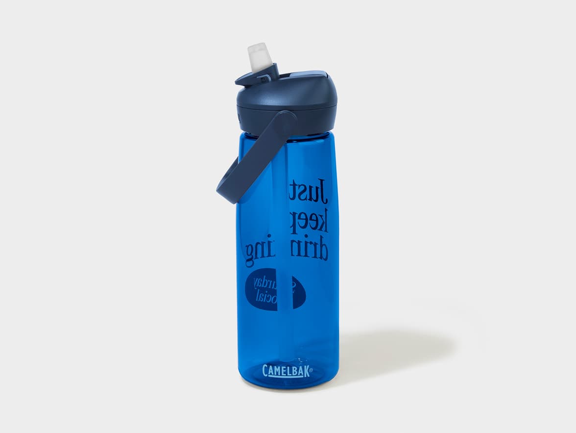A blue Camelbak water bottle with a dark blue cap and an exposed straw. The bottle has text on it that reads "Just keep drinking under social pressure" in reverse.
