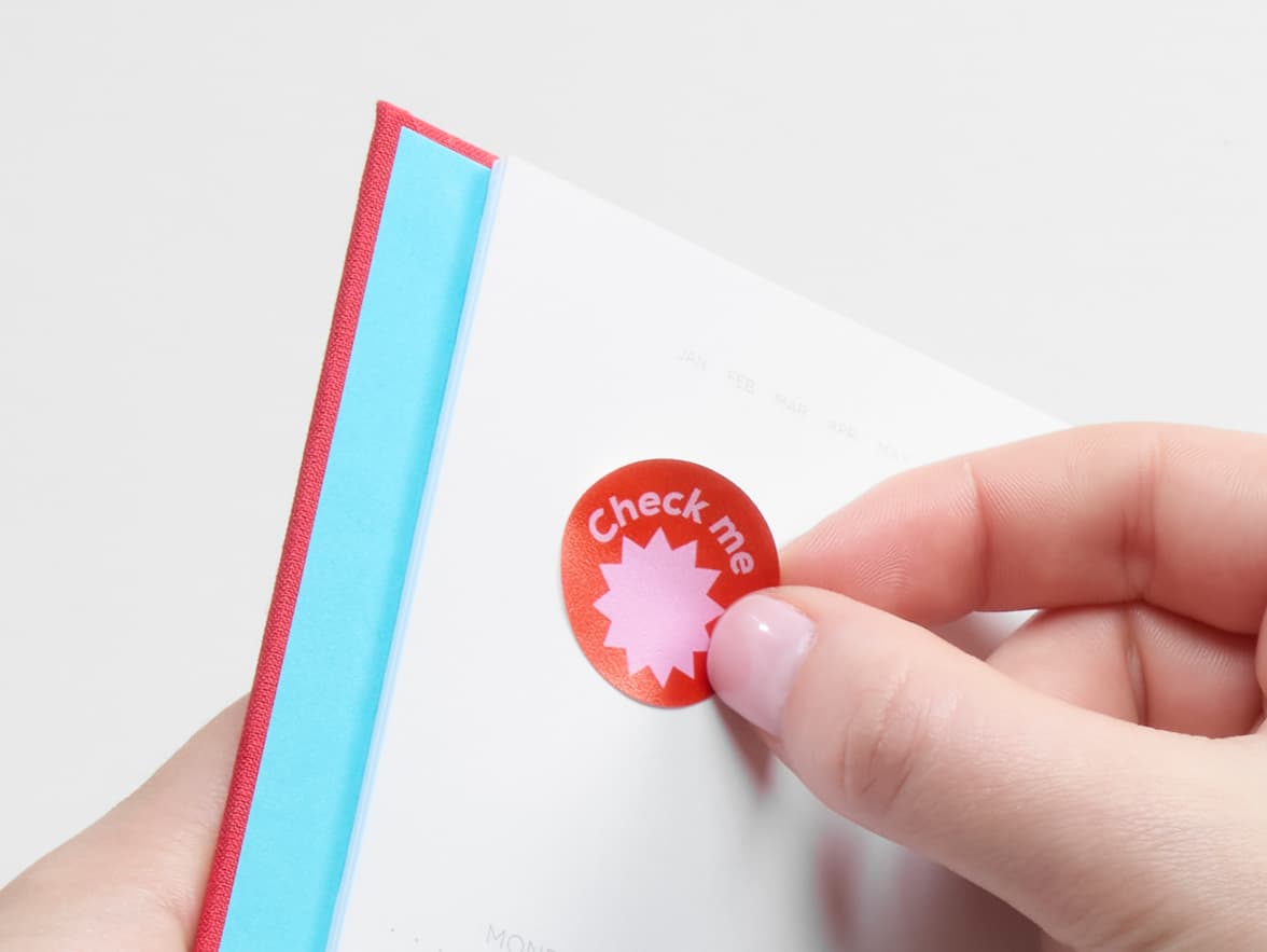 A person placing a customized round matte paper sticker in a notebook.