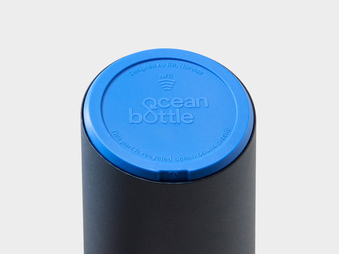 Top of an Ocean bottle with a blue lid that reads "Designed by K.B., Norway," "NFC" with a symbol, "Ocean bottle," and "This part is recycled ocean bound plastic."