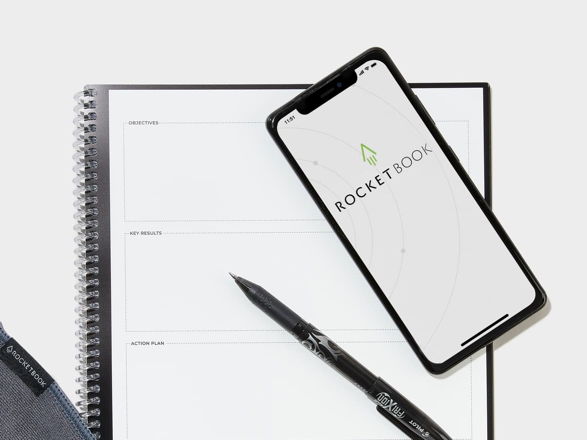 A Rocketbook notebook open to 'OBJECTIVES', 'KEY RESULTS', and 'ACTION PLAN' sections, with a smartphone displaying the ROCKETBOOK app and a Pilot Frixion pen.