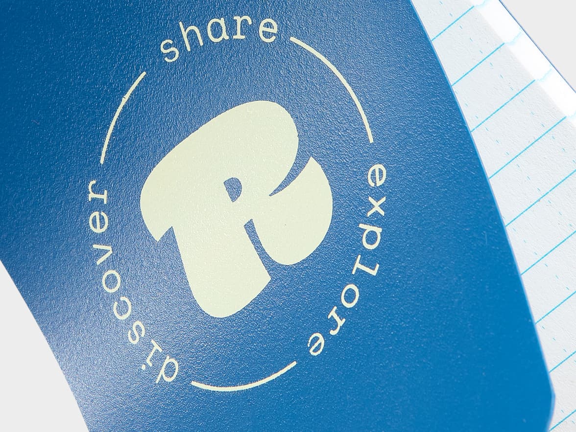 Blue notebook cover with a stylized "R" and the branding "share discover explore" in a circular layout.