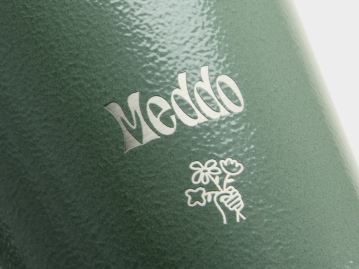 Close-up of a green, textured surface with a silver "Meddo" logo and a hand holding flowers icon.