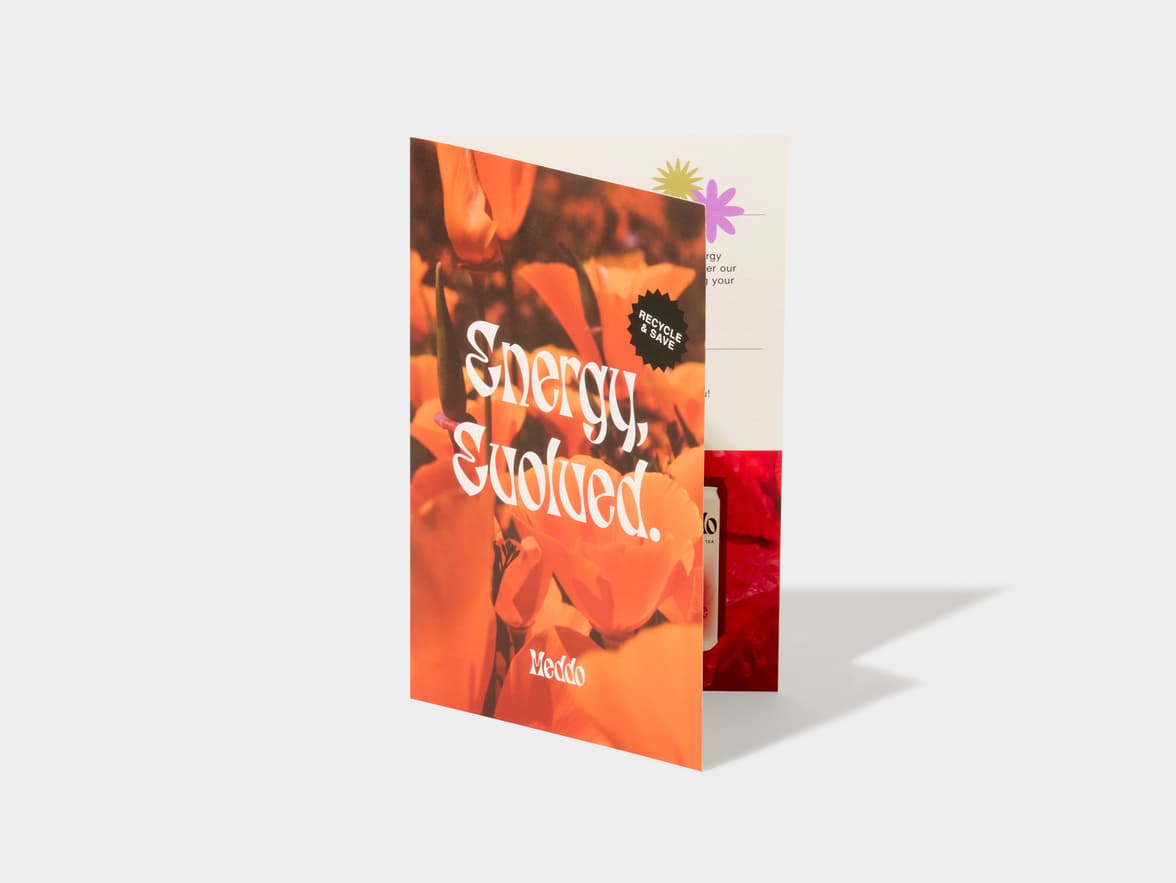 A folded brochure with orange flowers, text "Energy, evolved." and "Meddo", and a "RECYCLE & SAVE" sticker visible inside.