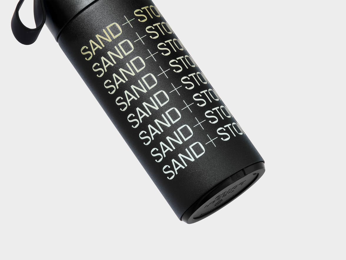 Black water bottle with "SAND + STONE" text repeated vertically.