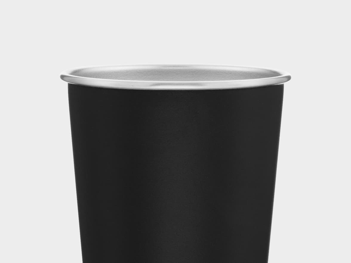 A close-up, top-down shot of a matte black reusable cup with a shiny silver rim, isolated against a light grey background.