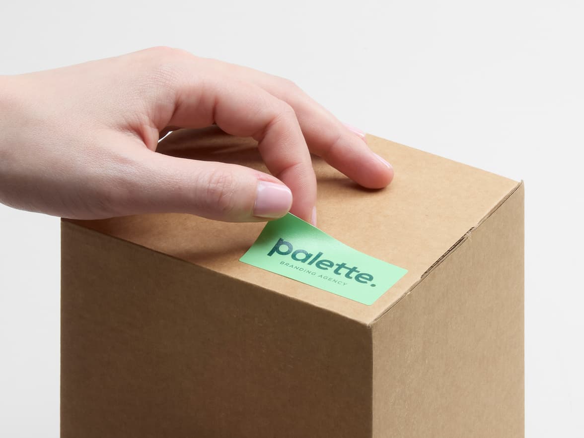 A person placing a matte paper sticker in size 1x2 on a cardboard box.
