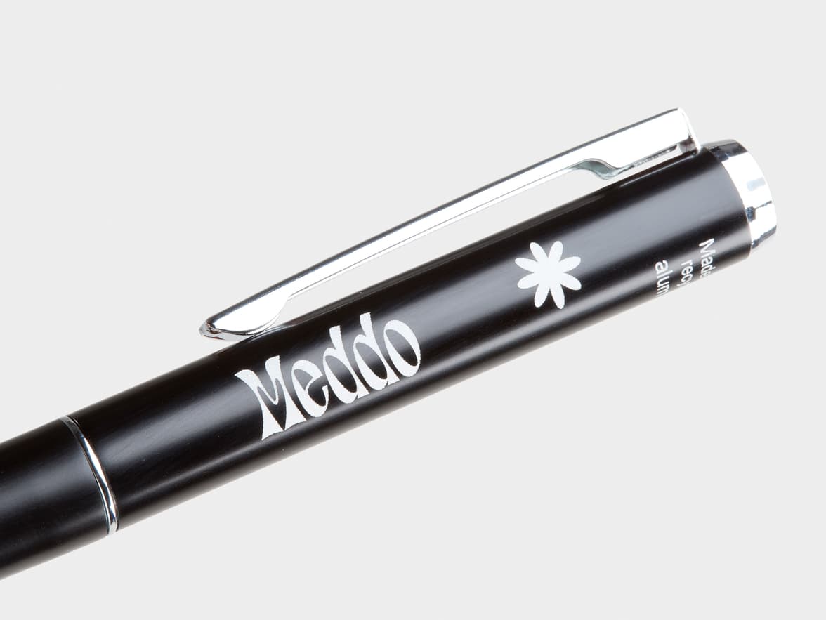 A black pen with a silver clip and accents, featuring "Meddo" branding, a white flower symbol, and vertical text "Made recy alum".