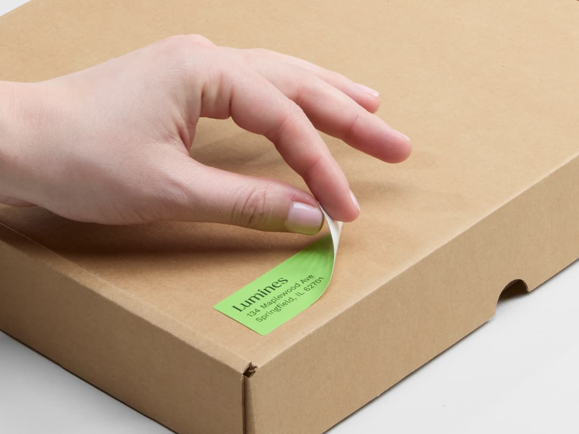 A person placing a customized matte paper sticker in size 1x2.75 on a cardboard box.