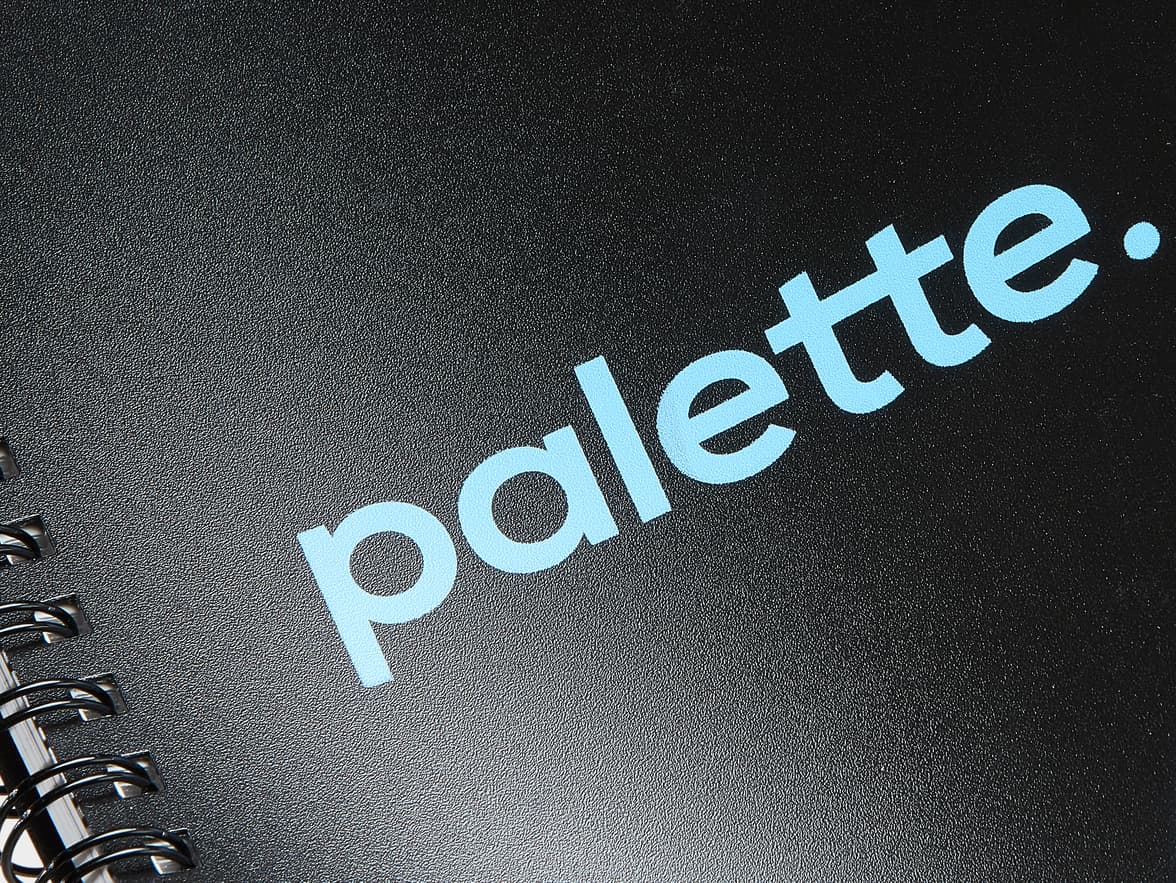 A black, textured, spiral-bound notebook with the brand name "palette." in light blue.
