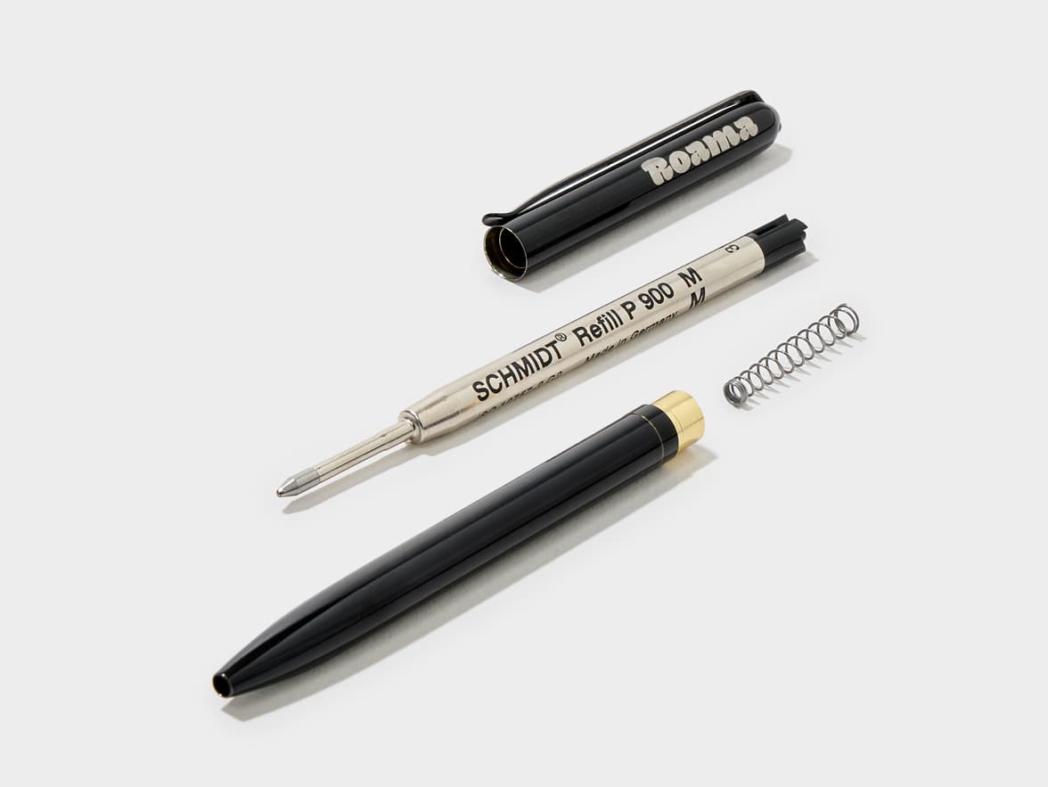 A black Roama pen disassembled, showing the cap, the main body with a gold-colored end, a spring, and a metal SCHMIDT® Refill P 900 M (Made in Germany).