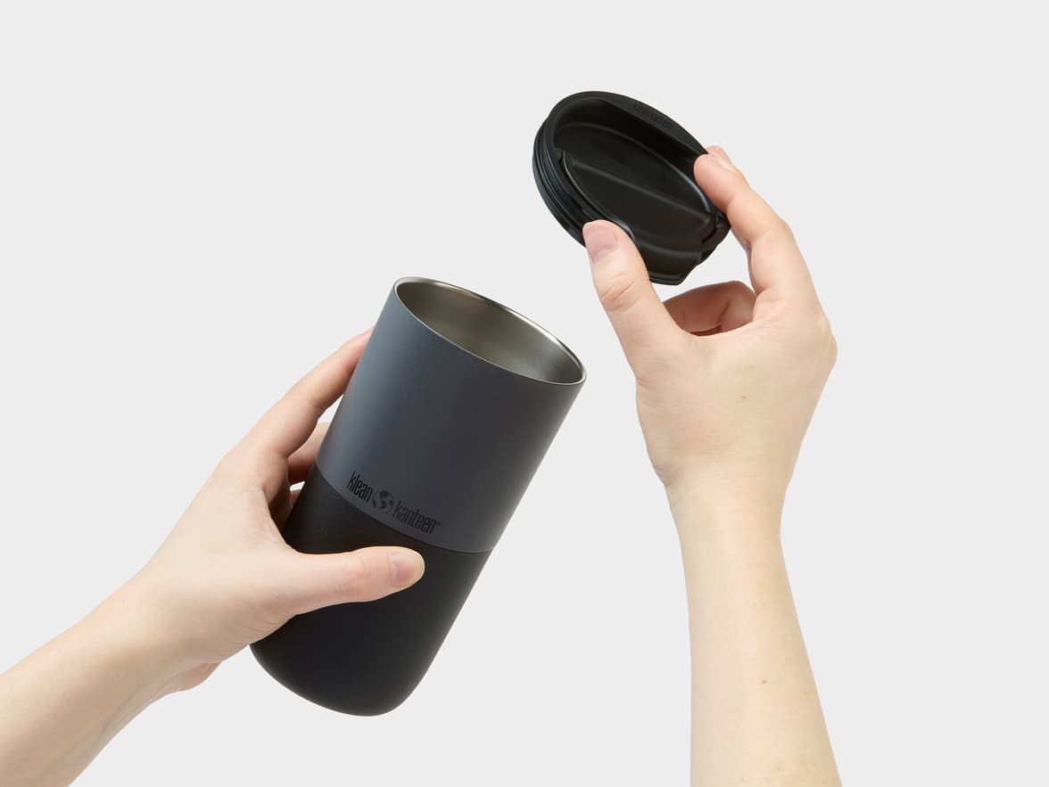 A pair of hands holding a dark gray Klean Kanteen tumbler with its lid removed.