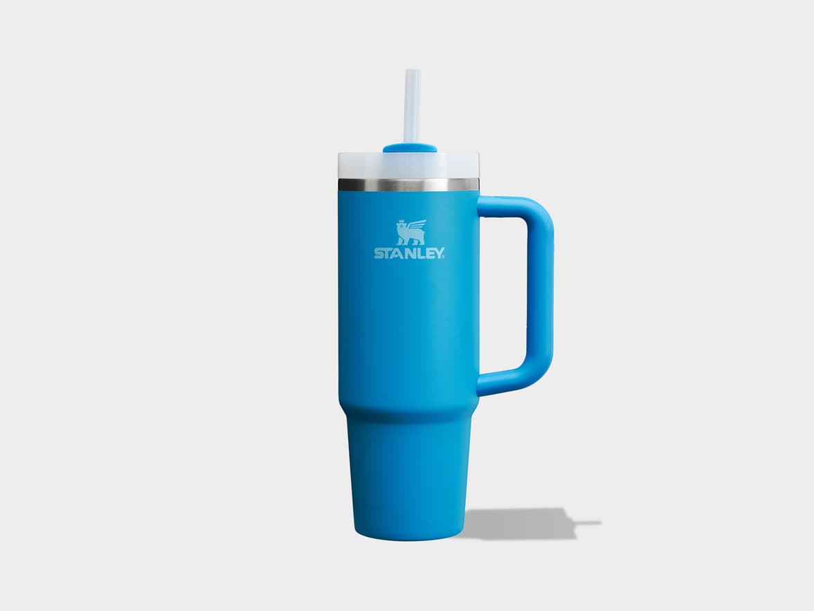 A blue Stanley tumbler with a handle and straw on a light background.