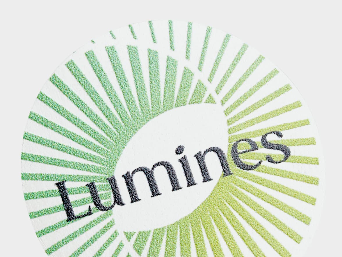 A close up image of a customized clear round sticker with a light green spiral circle and the word 'Lumines' printed on it.