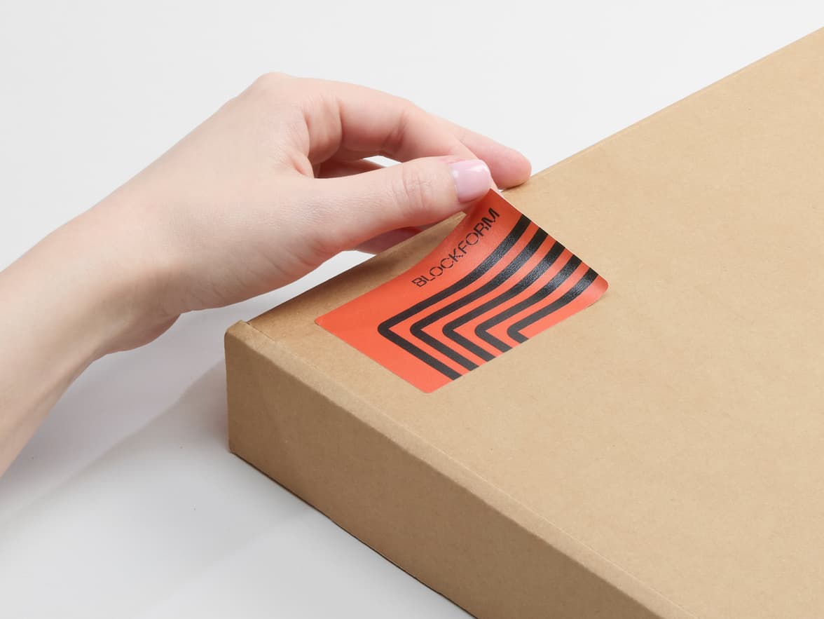 A person placing a customized matte paper sticker in size 3x2 on a cardboard box.