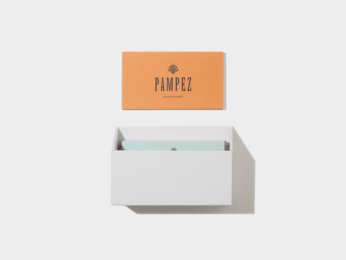 An orange card, branded 'PAMPEZ RESTAURANT' with a fan logo, rests above a white holder filled with light blue cards.