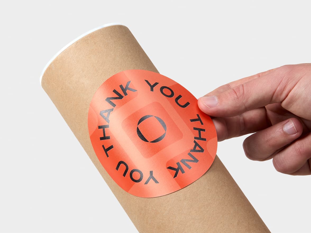 A hand placing a customized large round coated sticker onto a round packaging tube.