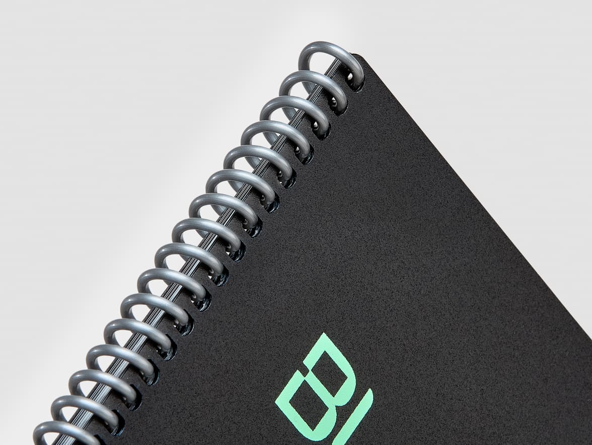 Close-up of a black spiral-bound notebook with a textured cover and a mint green "BI" logo.