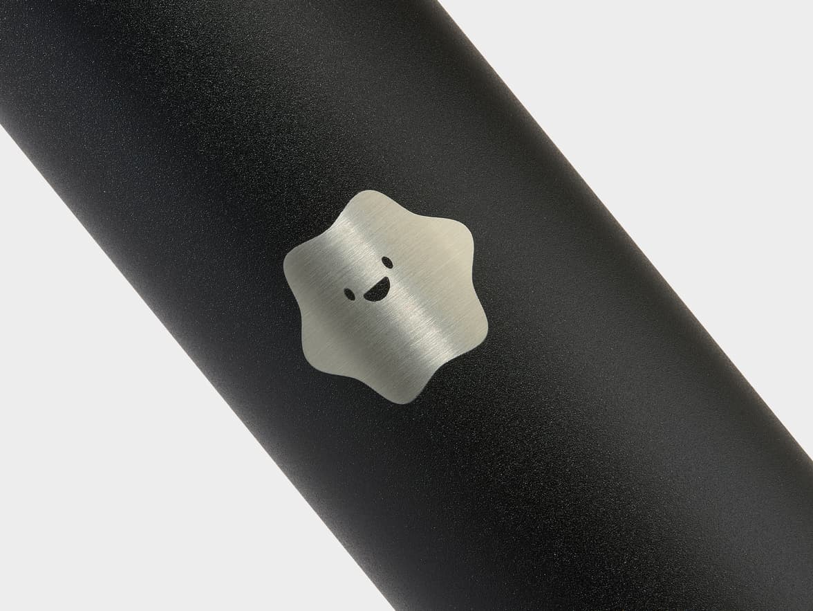 Black textured bottle with a silver, star-shaped emblem featuring a smiling cartoon face.