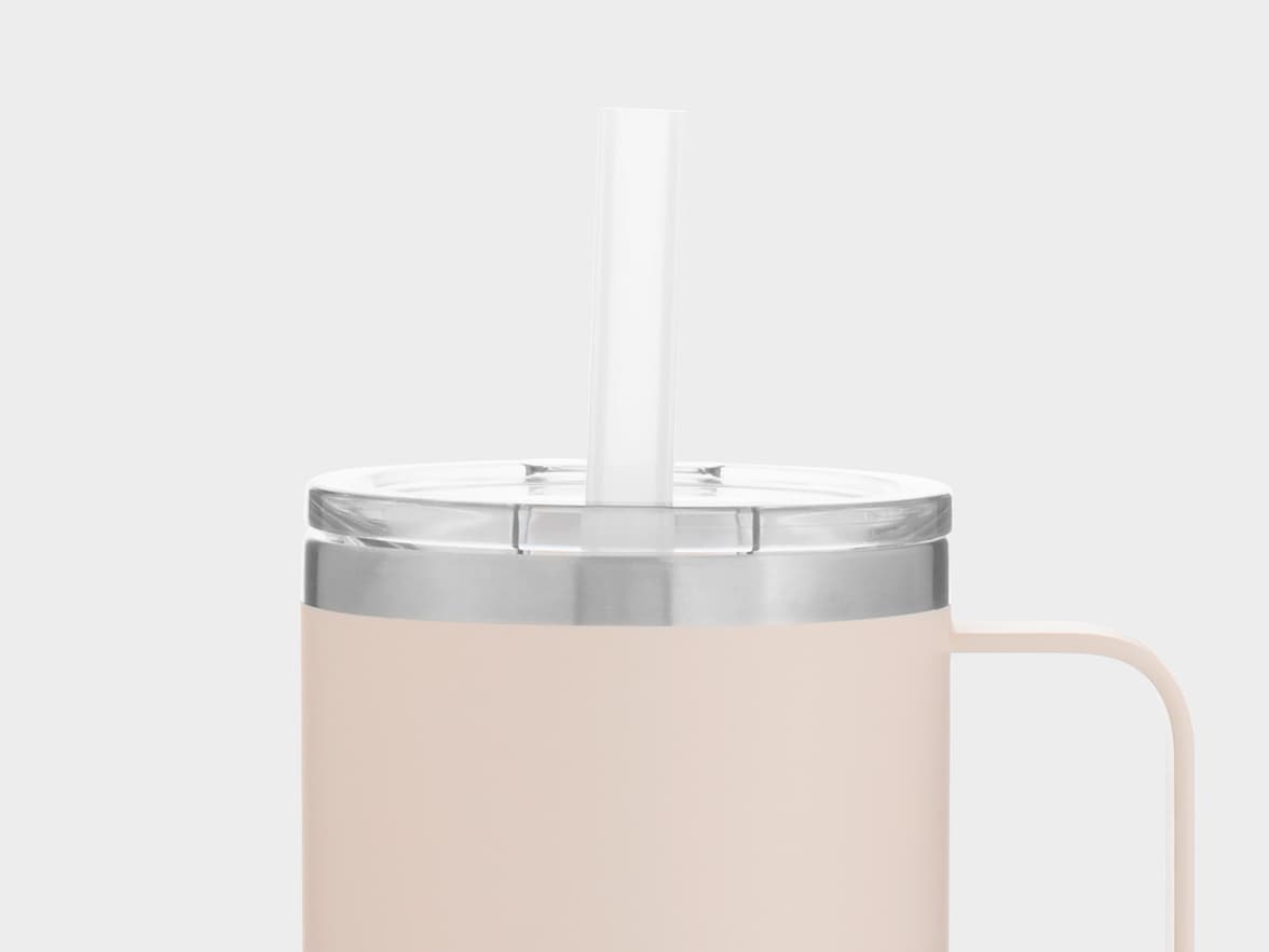 A close-up shot of a pale pink tumbler with a clear lid, a white straw, and a silver band. A portion of the matching handle is visible on the right side.