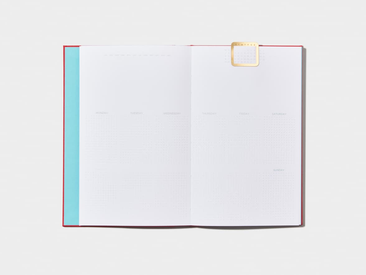 Opened Berry Red Cloth Planner with a calendar page inside and a gold clip 