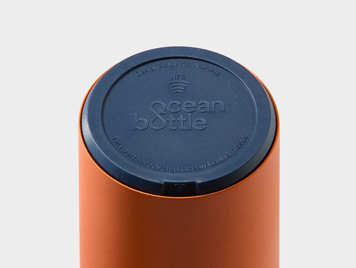An orange Ocean Bottle with a blue cap showing 'Designed by Ks, Norway', an NFC symbol, and 'This part is recycled ocean bound plastic'.