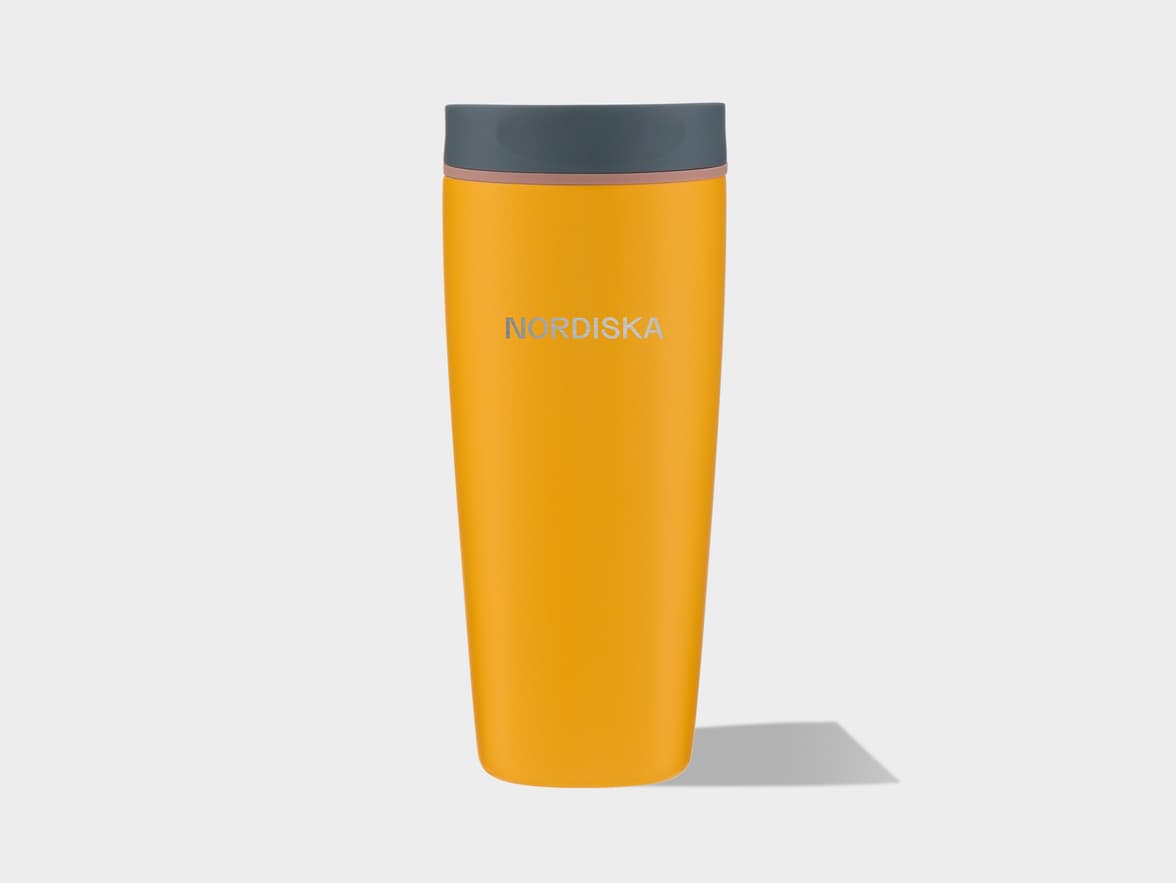 A yellow-orange travel mug with a dark gray lid and a thin pinkish-brown accent band. The brand name "NORDISKA" is inscribed in silver on the front. The mug stands upright on a light gray background, casting a subtle shadow.