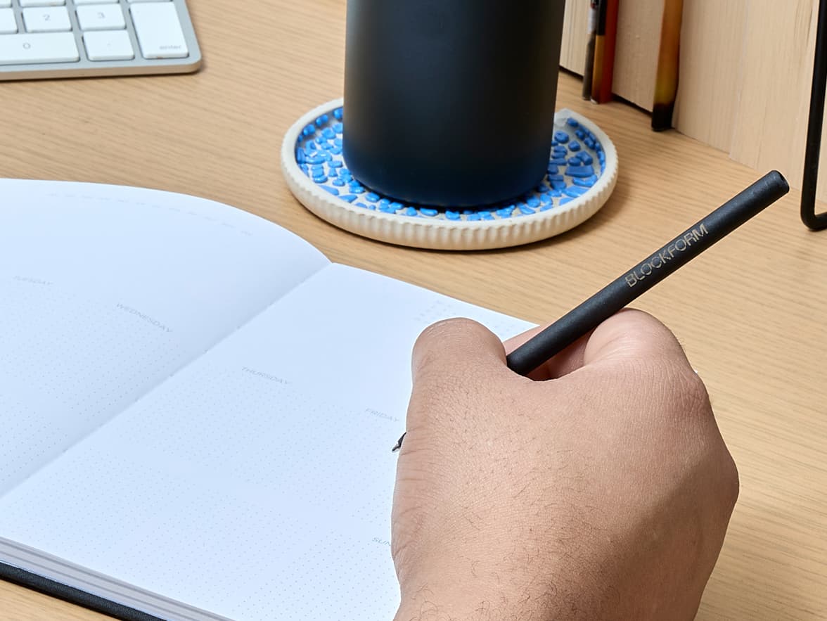 A hand holds a black BLOCKFORM pen over an open, dotted notebook.