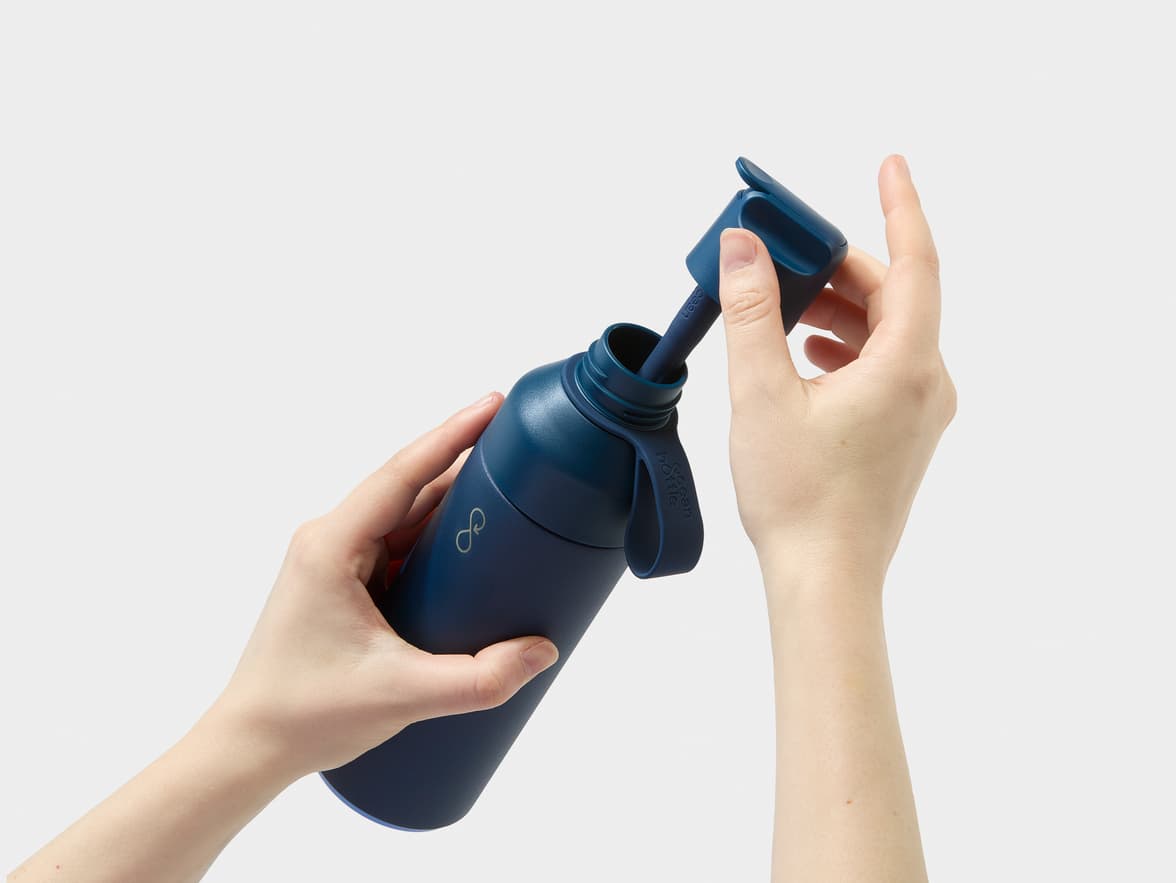 A person's hands opening a dark blue Ocean Bottle, revealing a straw.