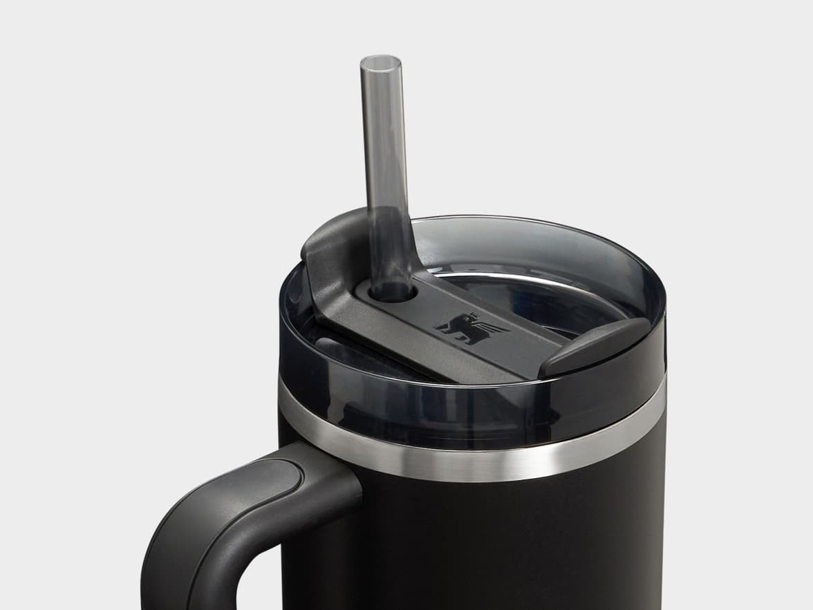 A close-up of a black Stanley Quencher FlowState tumbler, showing its clear lid, straw, and the Stanley winged bear logo.