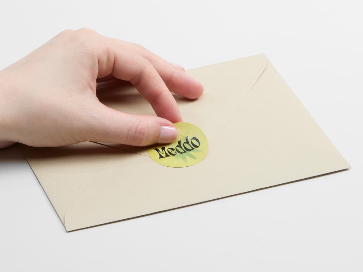 A person placing a customized round matte paper sticker in size 1.5 on an envelope.