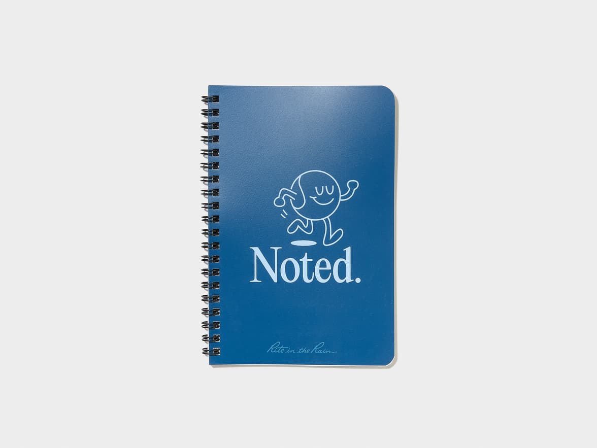 A blue spiral notebook featuring a white line drawing of a happy character, the text "Noted.", and "Rite in the Rain." branding.