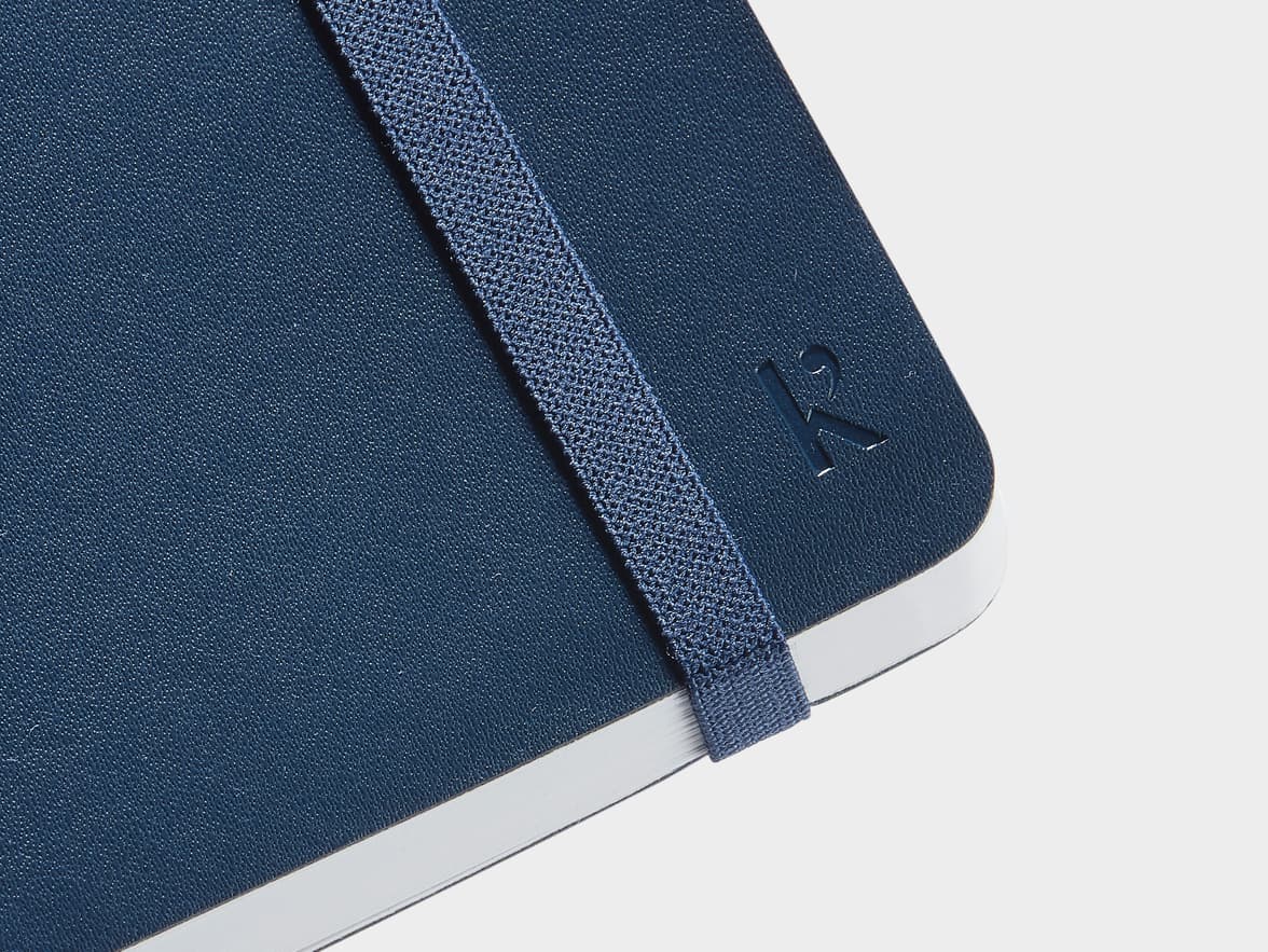 Close up shot of the corner of the cover of the Navy Karst Stone Paper Softcover Notebook with Karst branding and strap