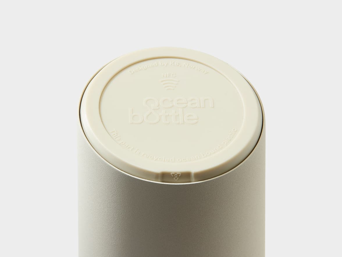 Top of an Ocean Bottle lid, light beige, with text "Designed by K8, Norway", "NFC", "Ocean Bottle", and "This part is recycled ocean bound plastic", plus a recycling symbol with "5".