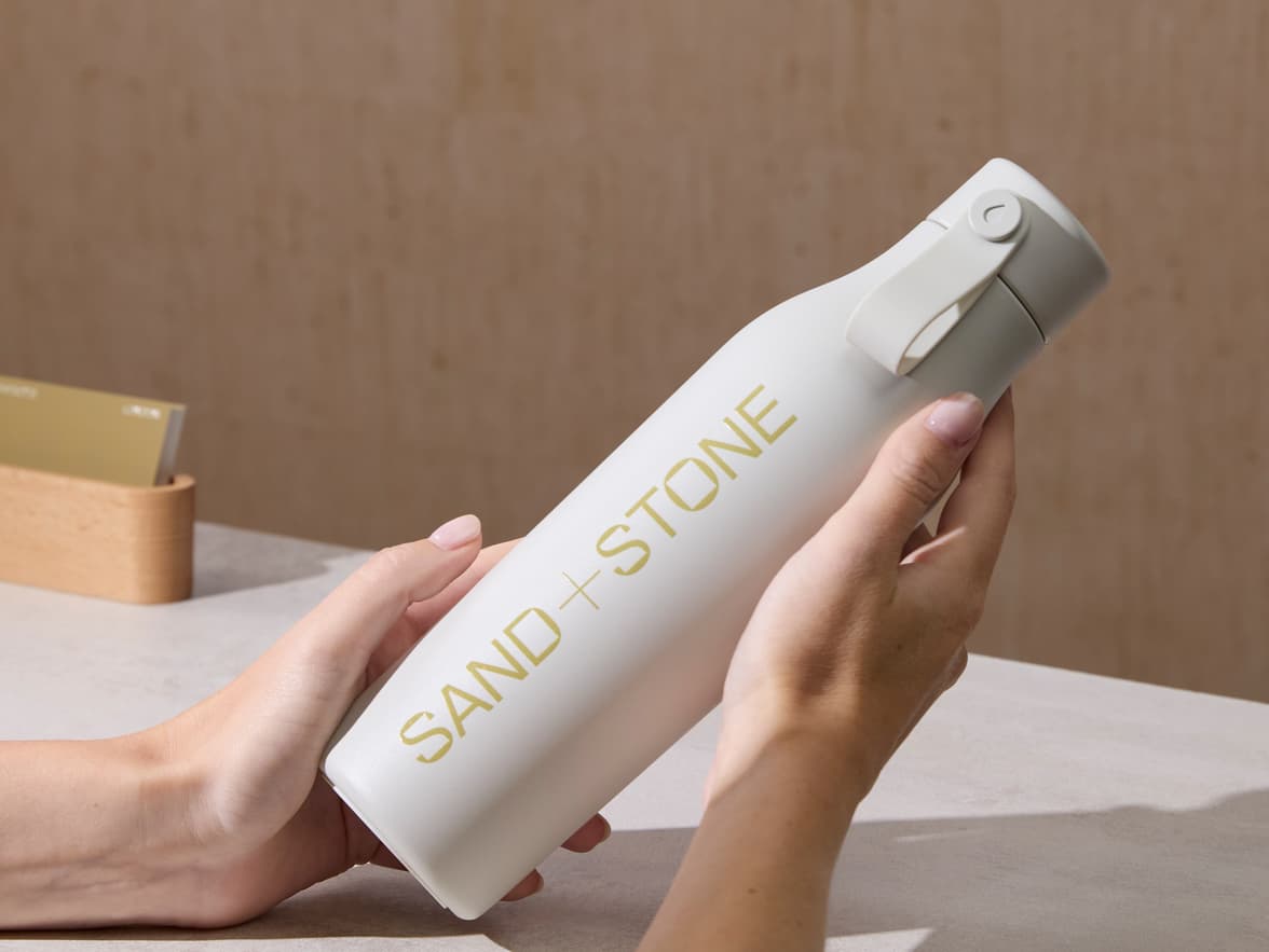 Person holding a cloud grey water bottle with custom gold branding.