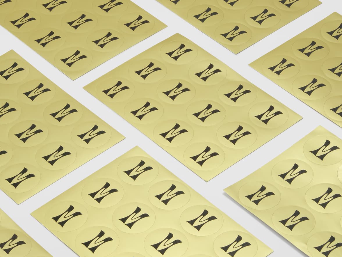 A collection of round gold metallic stickers with black branding on sheets.