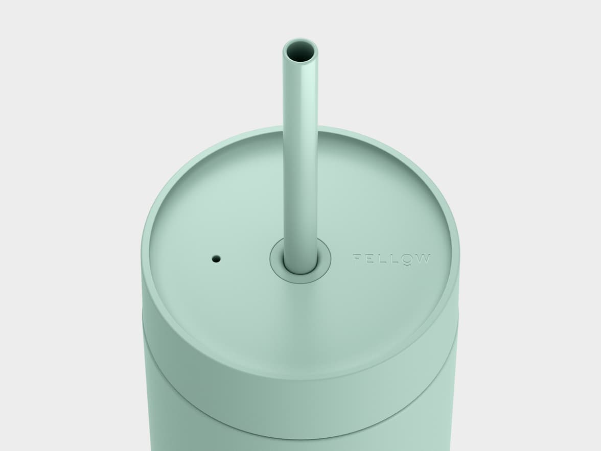 A top-down, close-up view of the mint green lid and straw of a tumbler. The lid has a circular opening for the straw, a small vent hole, and the word 'FELLOW' embossed on its right side.