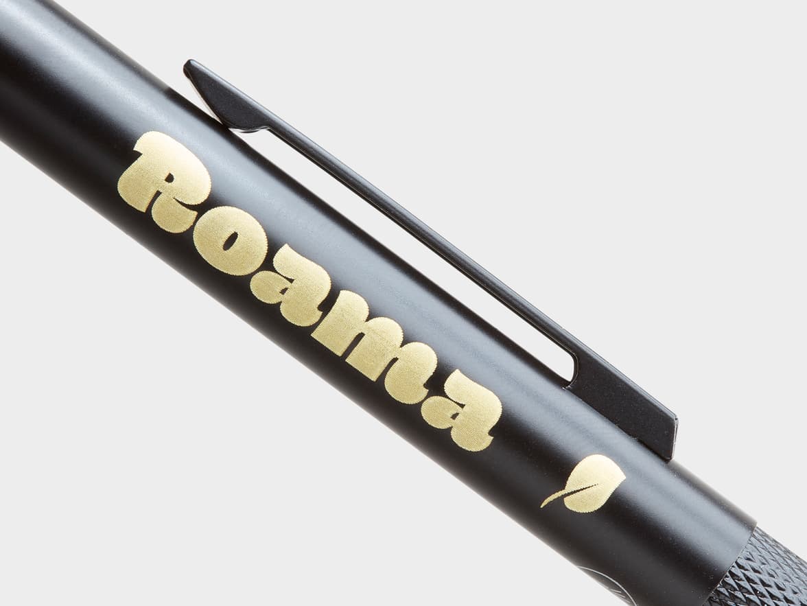 Black pen with textured gold 'Roama' branding and a leaf symbol.
