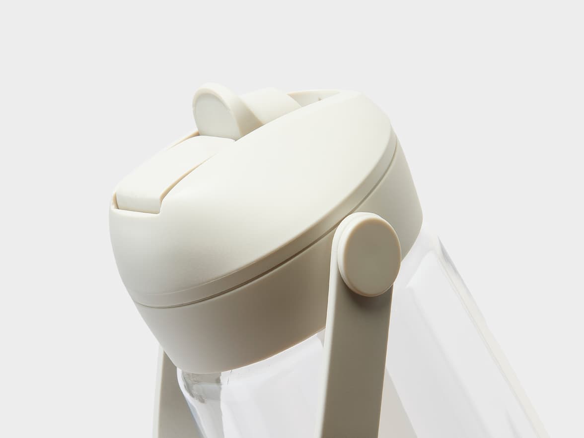 Close-up of the upper part of a clear bottle with a light beige flip-top lid and a matching handle on a white background.