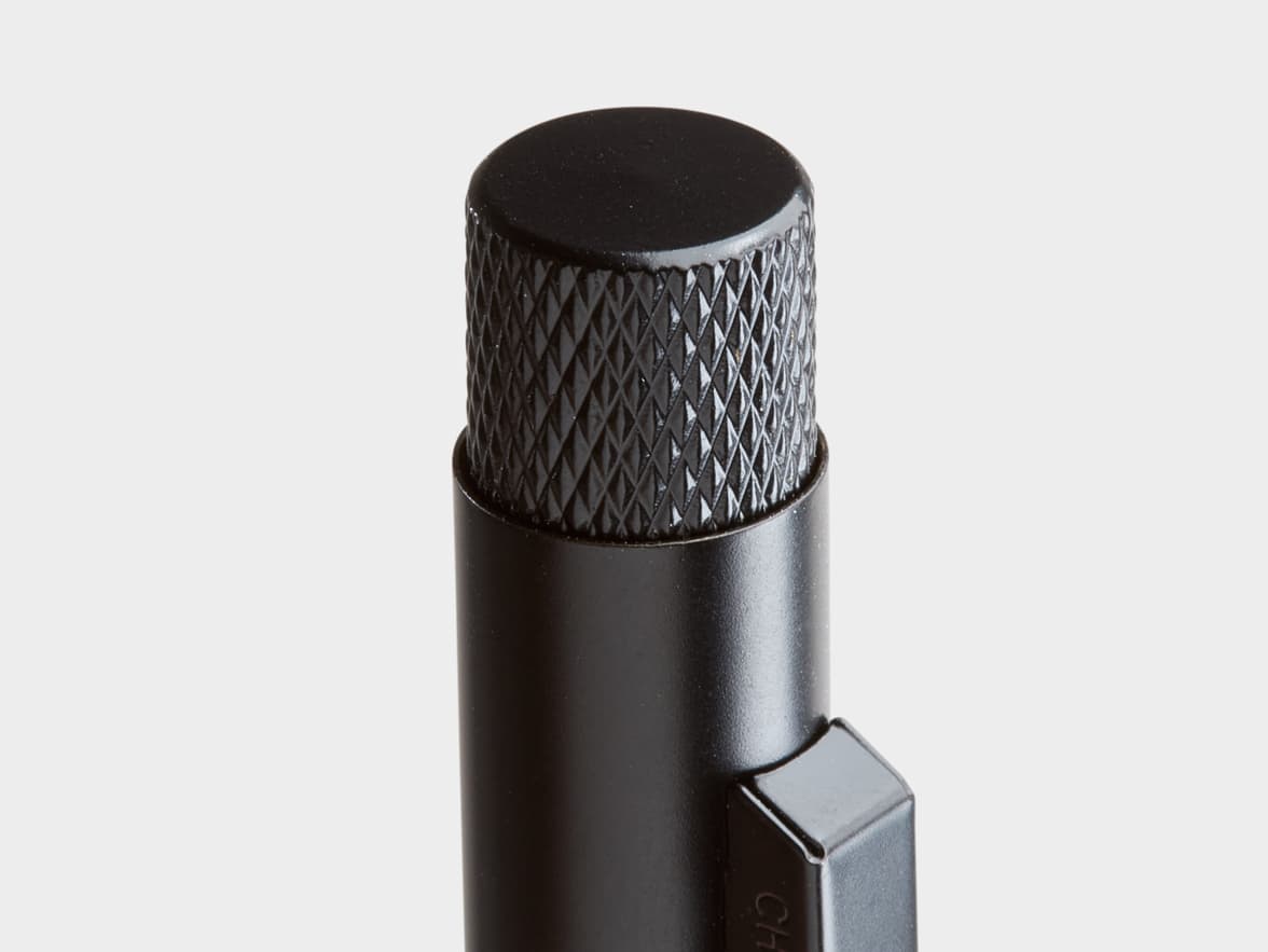 Close-up of the top of a black metallic pen or pencil with a knurled top and a clip marked "CH".