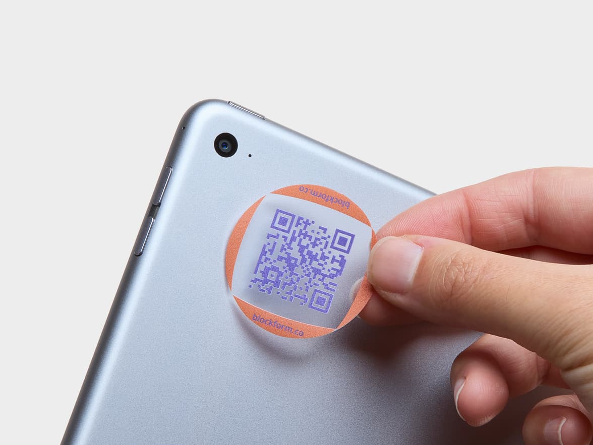A hand placing a customized clear sticker with a purple QR code onto a laptop.