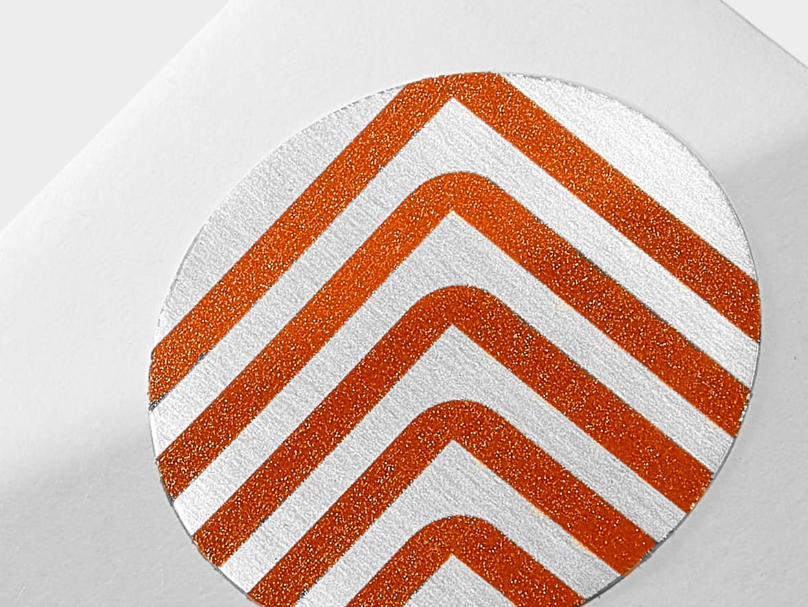 A close up image of a round silver metallic sticker with orange customization.