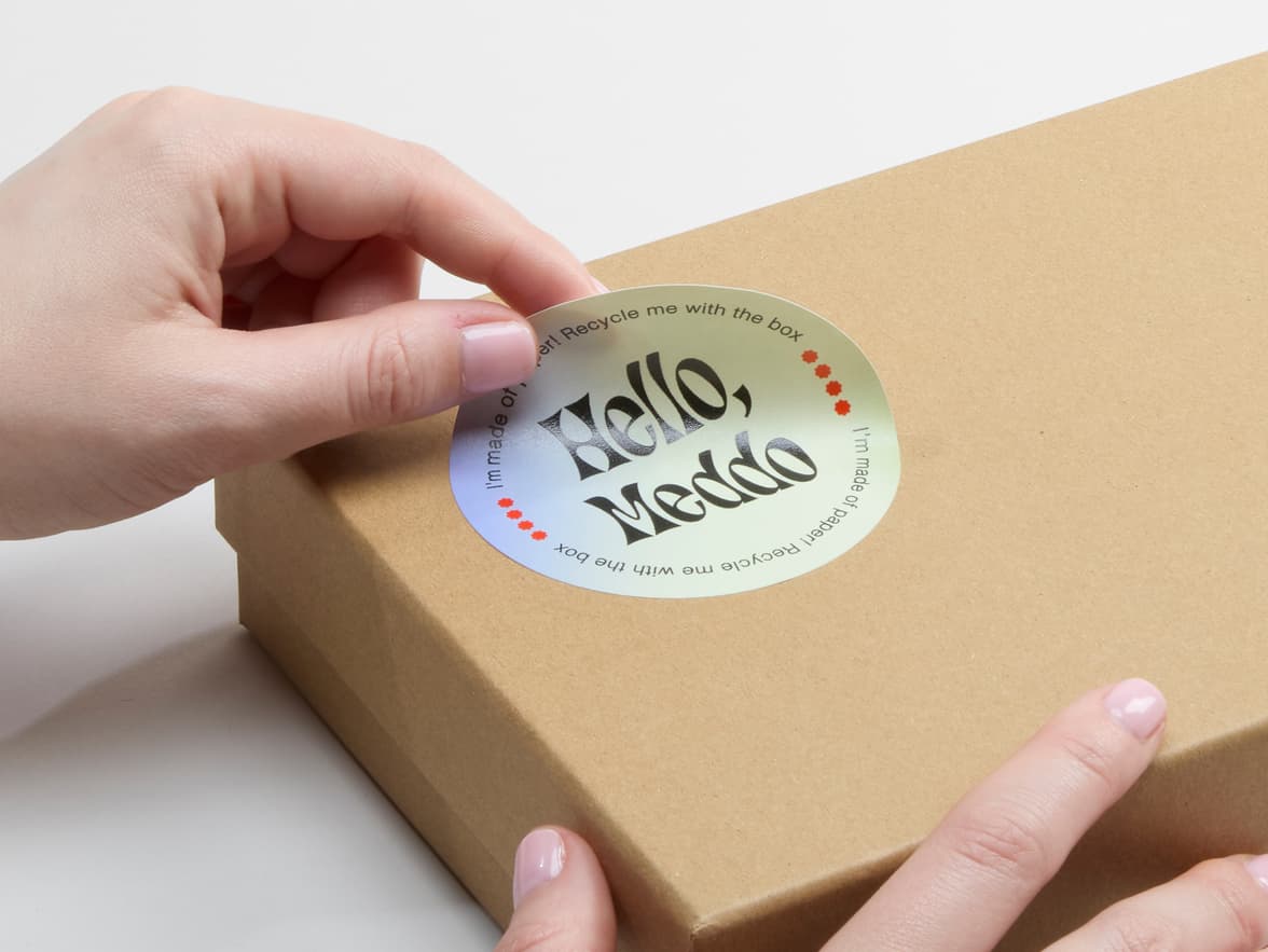 A person placing a customized matte paper sticker in size 3 inch on a cardboard box.