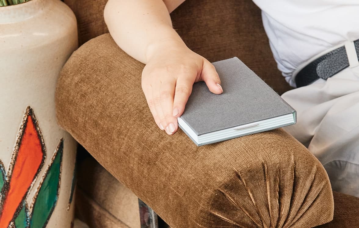 A person sat on a couch with their arm on the arm rest, holding a customized notebook.