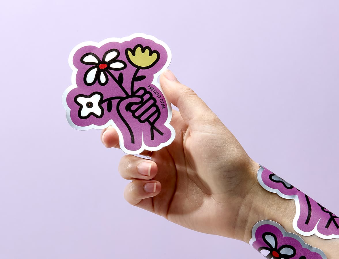 A hand holding a customized sticker with more stickers stuck onto their wrist.