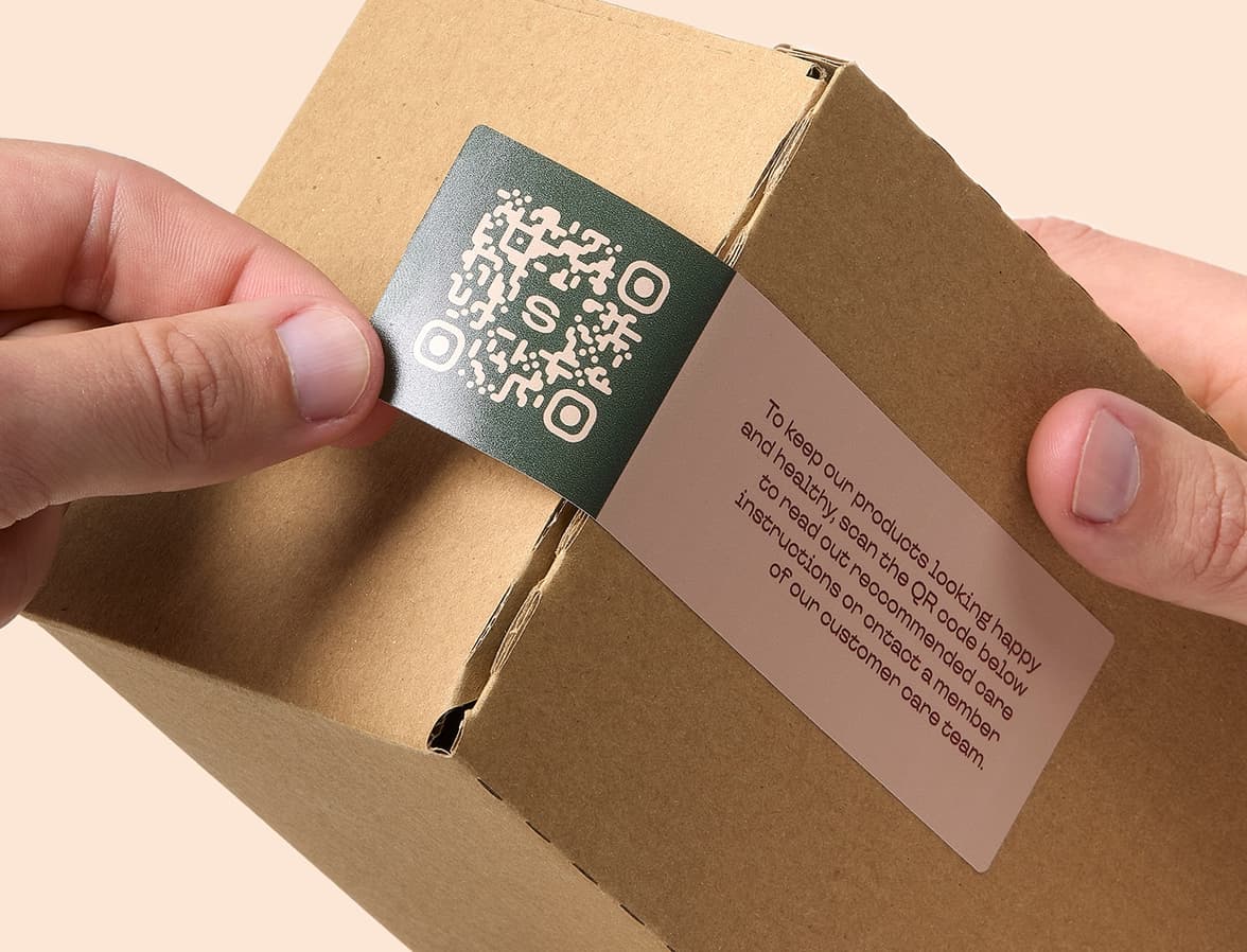 Hands placing a customized rectangular coated sticker on the corner of a cardboard box.