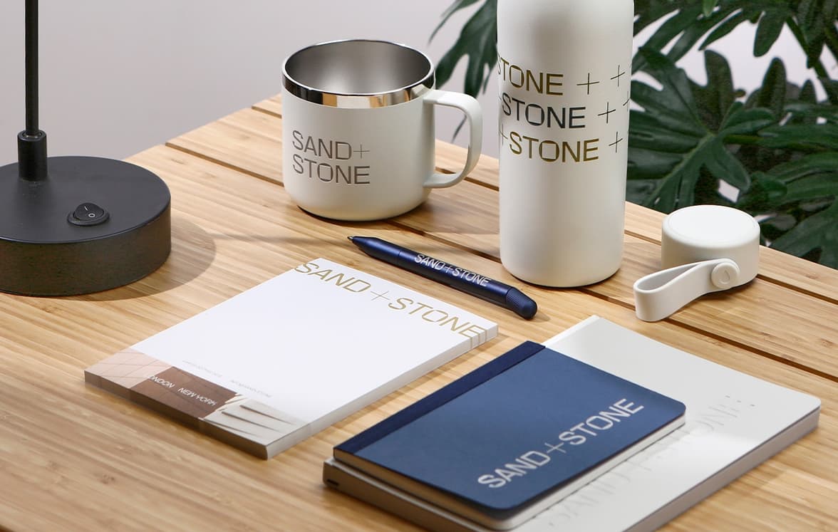 A collection of various branded merchandise products including notebooks, drinkware and a pen.