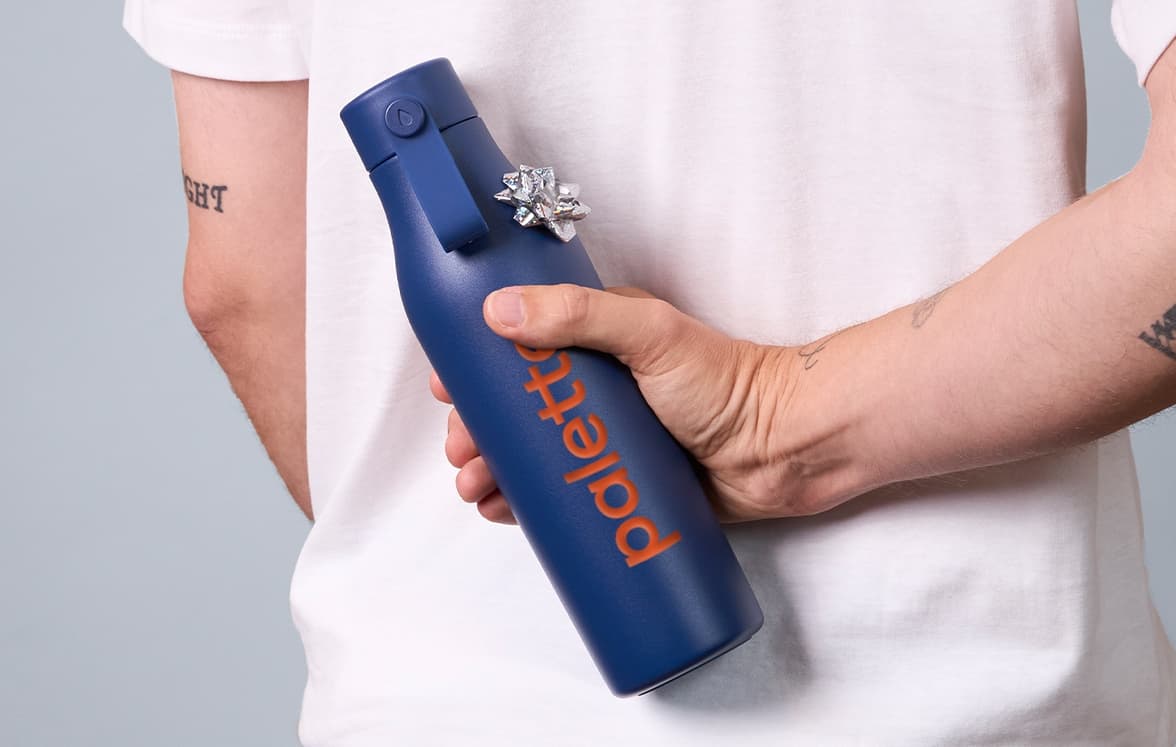 A person holding a customized water bottle with a gift tag on it behind their back.