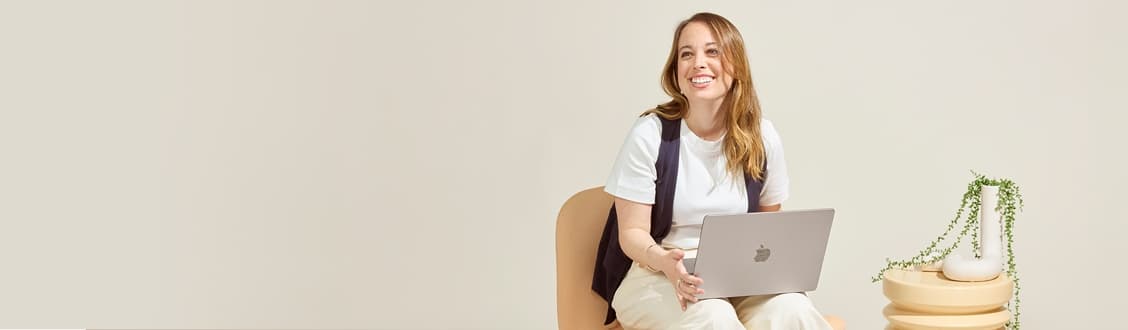 A woman sat with an open laptop on her lap whilst looking over to the left hand side of the image.